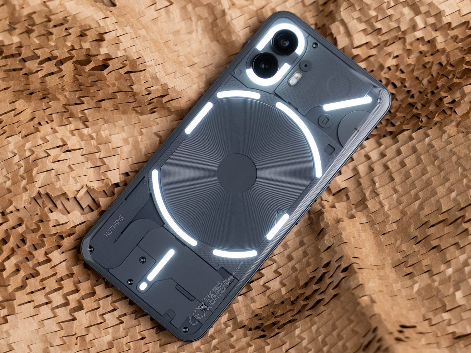 Nothing Phone (2), auf dem Display liegend, zeigt seine transparente Rückseite mit aktivierter Glyph-Beleuchtung.