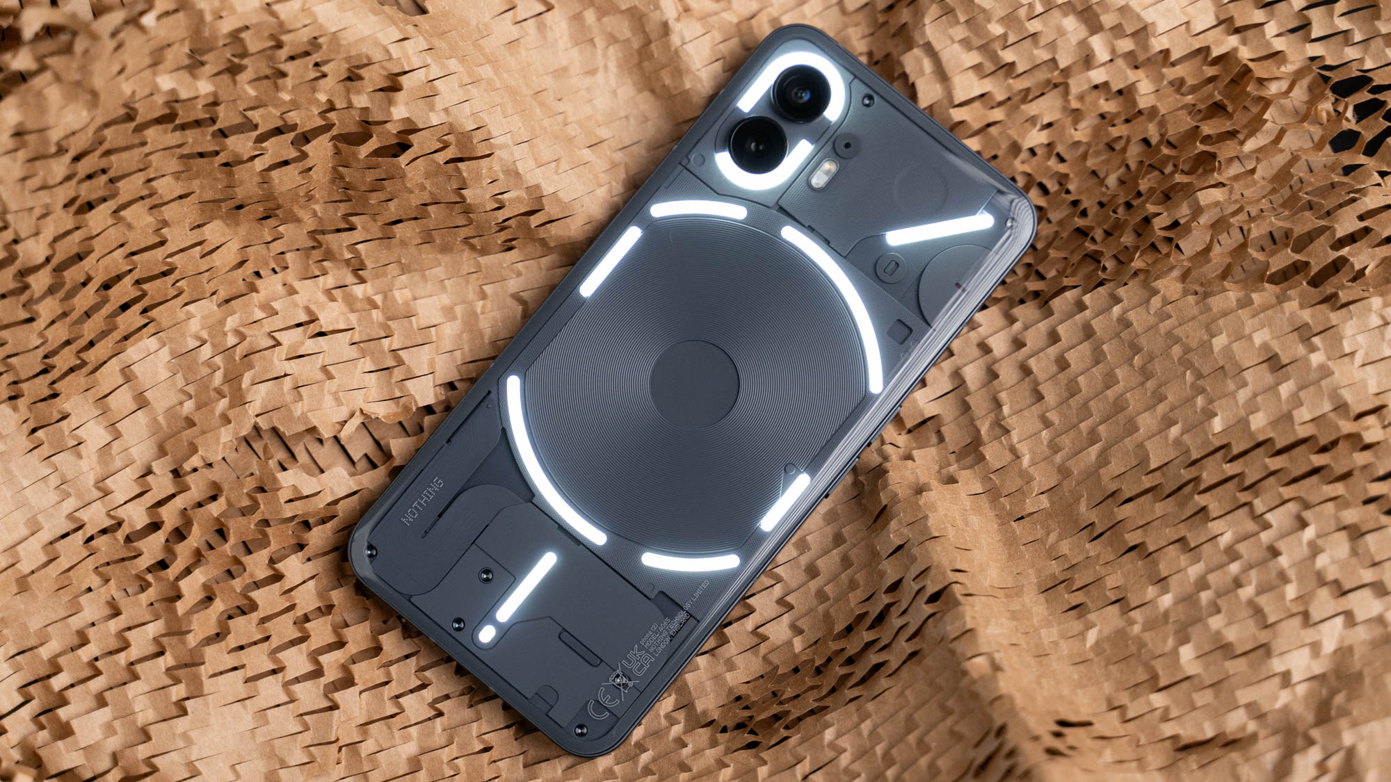 Nothing Phone (2), auf dem Display liegend, zeigt seine transparente Rückseite mit aktivierter Glyph-Beleuchtung.