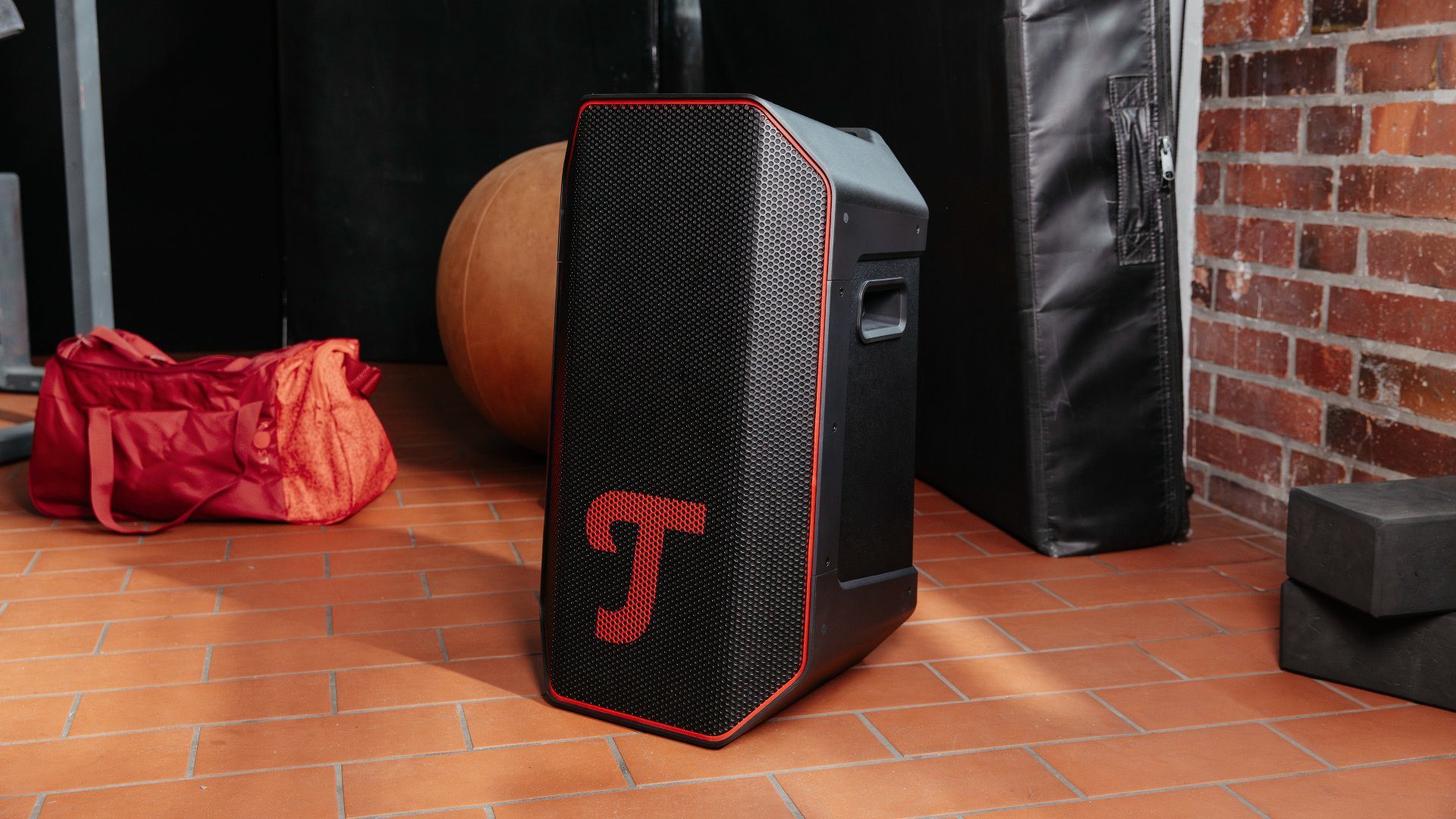 Teufel Rockster Air 2 Lautsprecher in einem Zimmer mit Holzboden. Daneben orangefarbene Tasche.