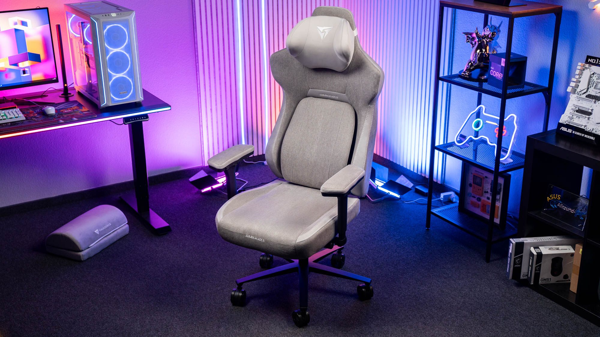 Grauer Gaming-Stuhl mit Stoffbezug vor bunter Beleuchtung und Schreibtisch