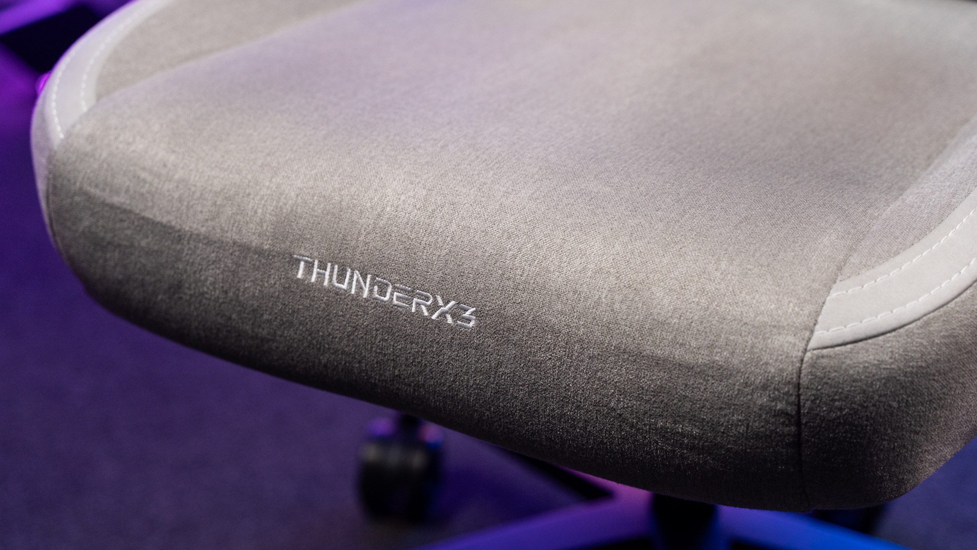 Grauer Stoffbezug auf Sitzfläche eines Gaming-Stuhls mit Schriftzug "ThunderX3"