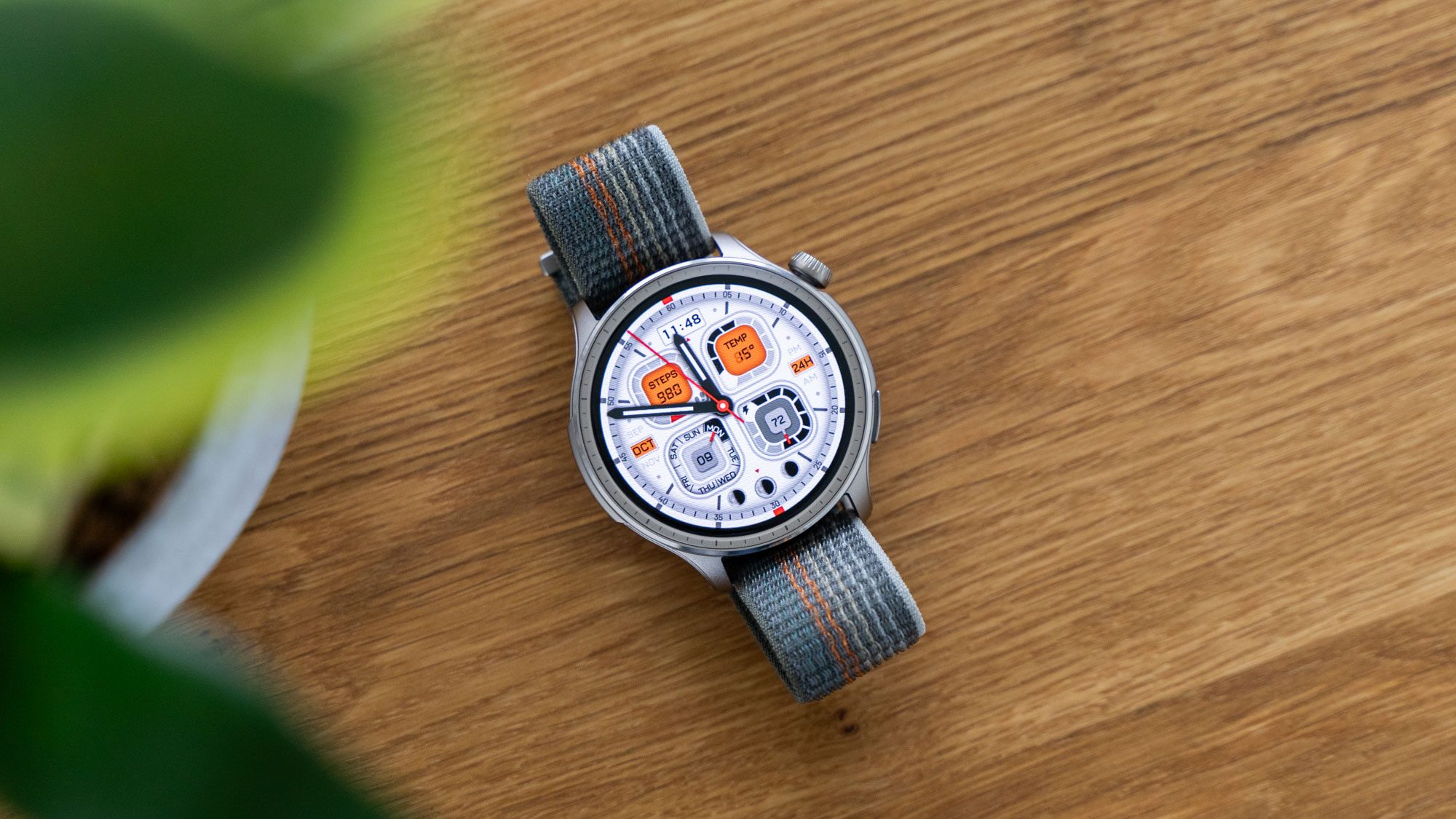 Amazfit Balance Smartwatch liegend auf einem Holztisch mit eingeschaltetem Display und hellem Ziffernblatt.