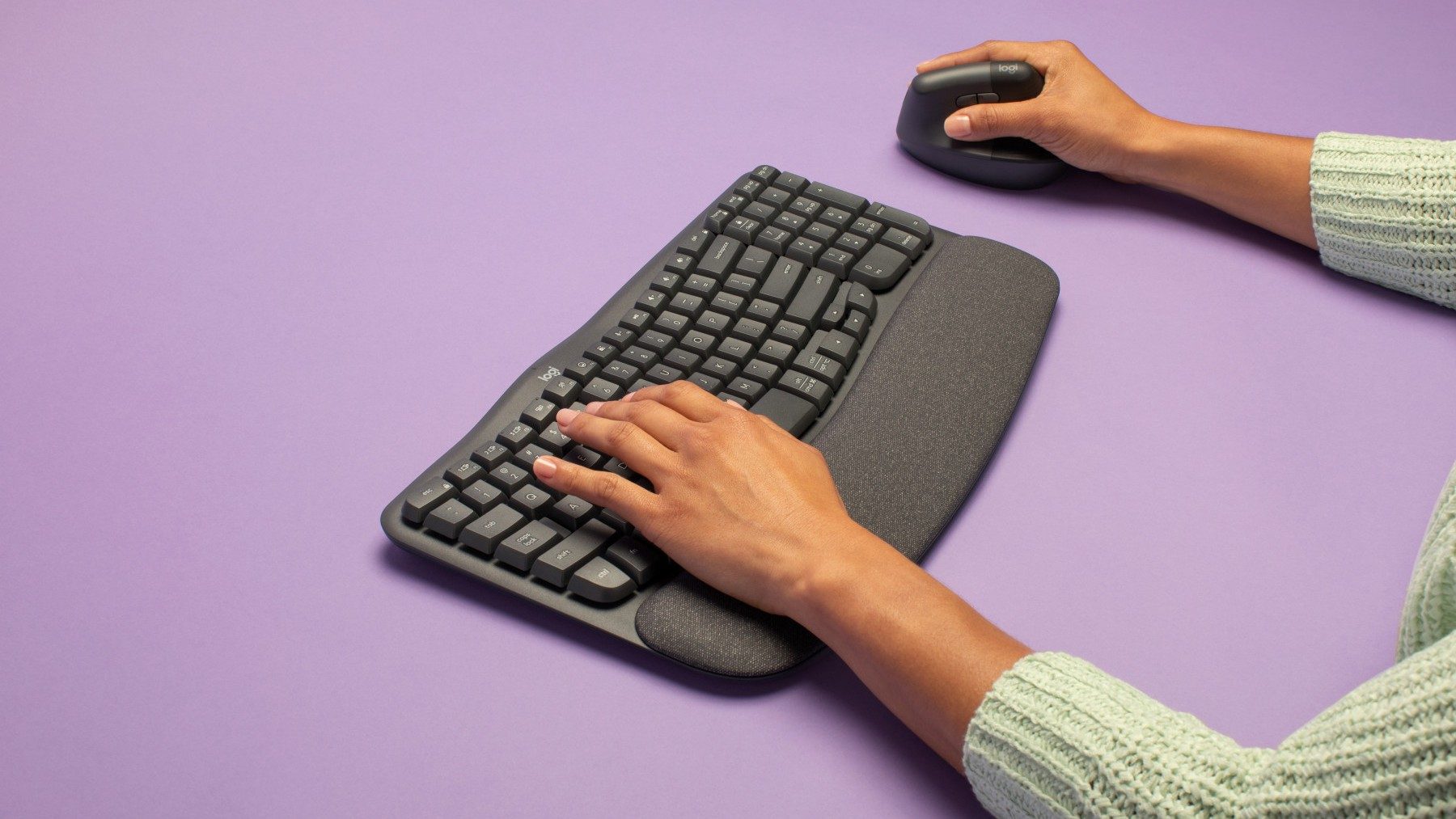 Logitech Wave Keys Tastatur auf violettem Untergrund mit Händen.