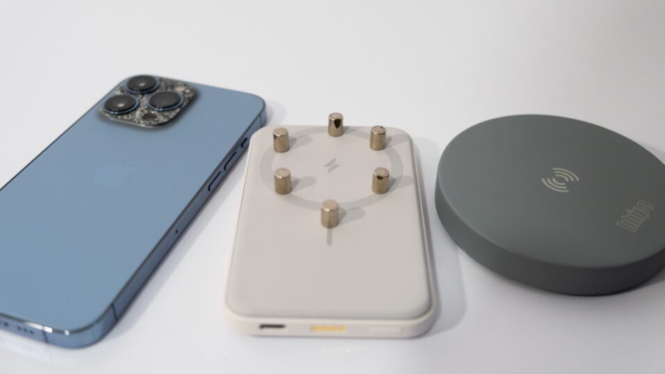 Foto zeigt blaues iPhone 13 Pro links, mittig eine Anker MagGo-Powerbank mit Magneten drauf, rechts ein Qi-Ladepad.