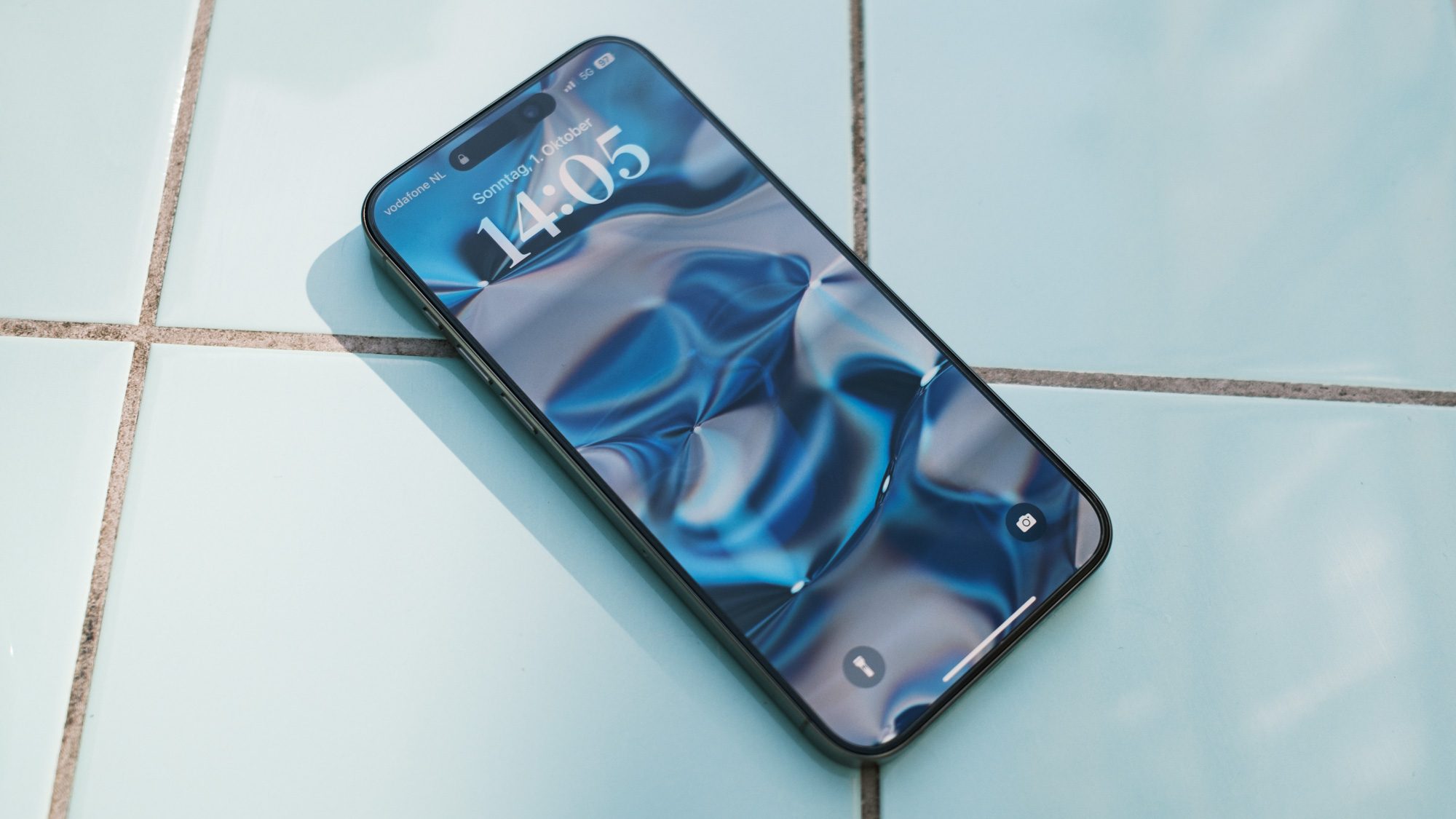 Apple iPhone 15 Pro Max auf blauen Fließen mit Sperrbildschirm.