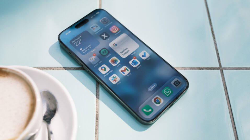 Apple iPhone 15 Pro Max auf blauen Fließen mit Startbildschirm.