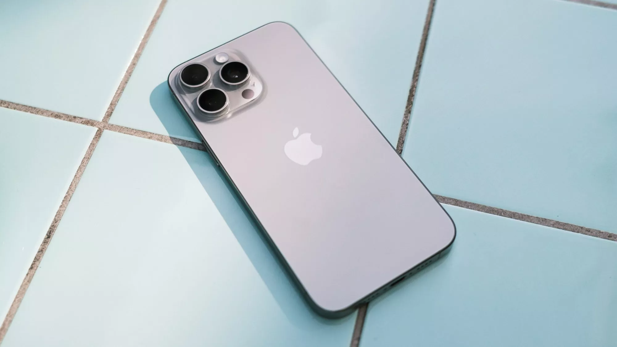 Apple iPhone 15 Pro Max auf blauen Fließen mit Rückseite in Titan Natur.