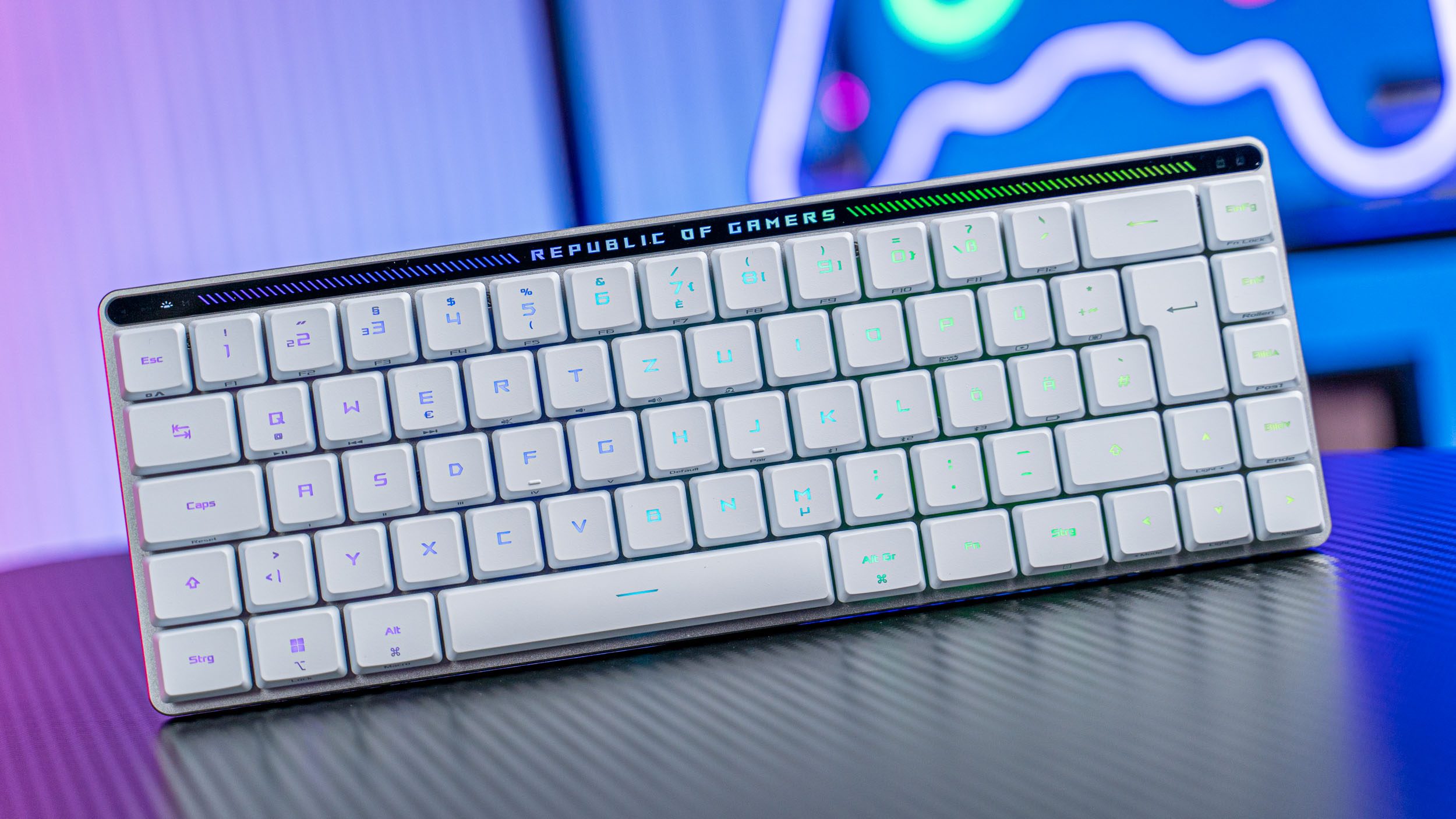 Weiße Asus ROG Falchion RX Low Profile Gaming-Tastatur auf Tisch mit Carbonoptik, dahinter bunte Beleuchtung.