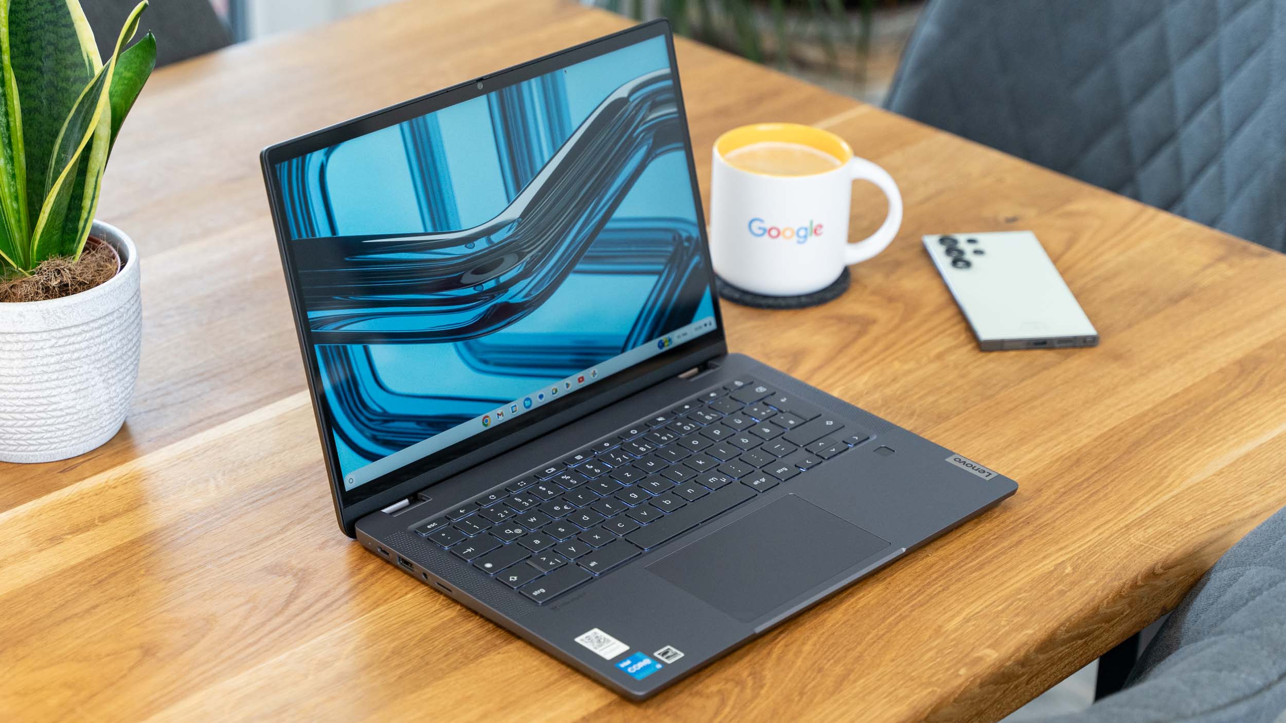 Lenovo IdeaPad Flex 5i 14 Chromebook Plus auf Holztisch mit Kaffeetasse dahinter.